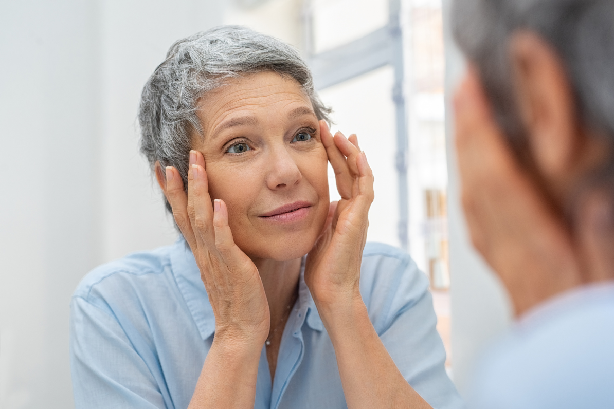 Elderly lady looking at her self in the mirror and touching the corners of her eyes after receiving botox